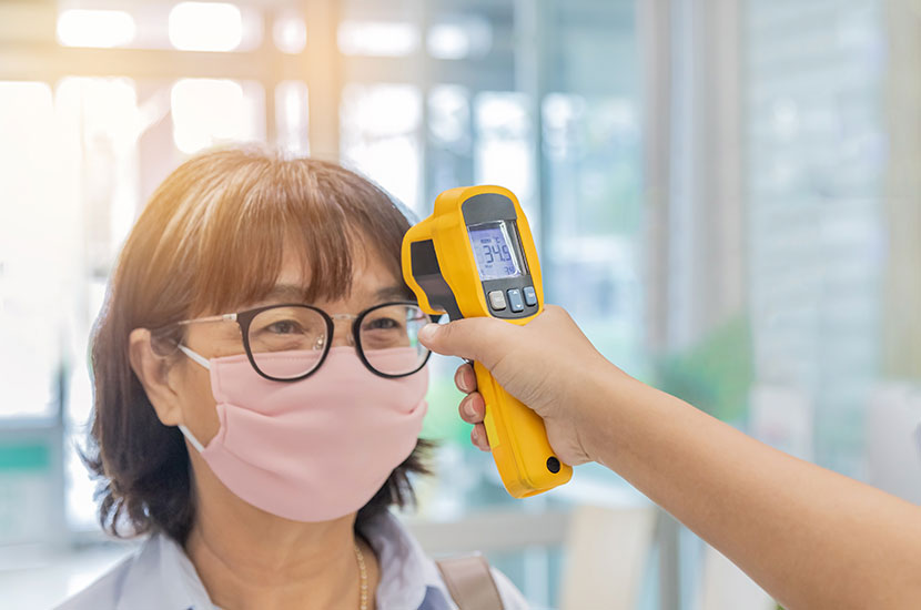 Security guard using digital medical electronic thermometer measures checking body temperature screening passengers